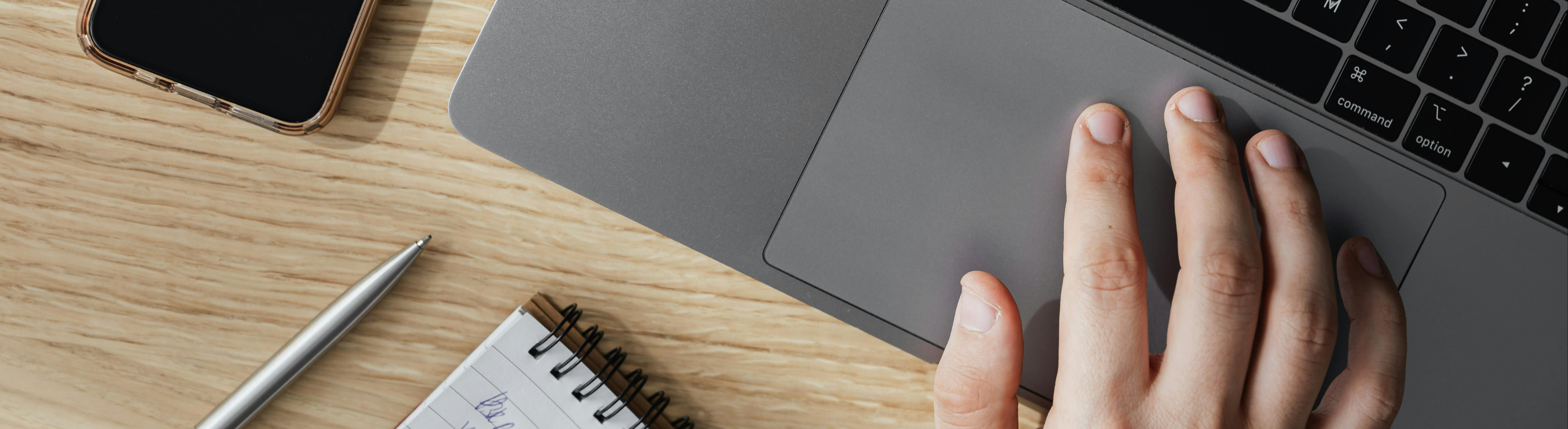 Person working on laptop at table with smartphone and notepad