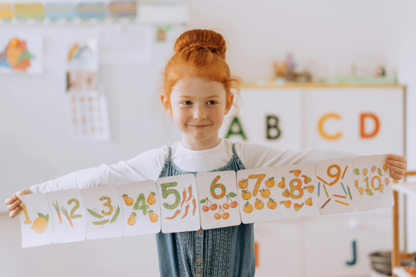 A Girl in the Classroom Holding a Paper Banner with Numbers