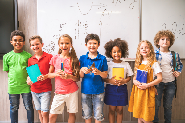 children holding school supplies in front of whiteboard