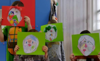 Four children holding up abstract art work depicting their faces in front of their face.
