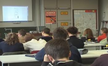 a secondary CLIL science class with a group of teens seen from the back all facing the board