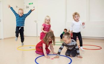 Photo of kindergarten children playing a core PTLM game.  Two children are visiting a hoop with a letter in it.  Other children are travelling to the hoop. The are all engaged in the game.