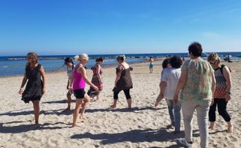 A group of teachers taking part in a well-being movement activity on the beach.  They are walking barefoot with the sea in the background.