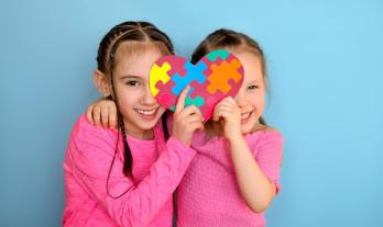 Sisters holding a heart-chaped card with puzzle pieces inside