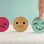 Smiley, neutral, and frowny faces made of paper, smiley being chosen by a hand